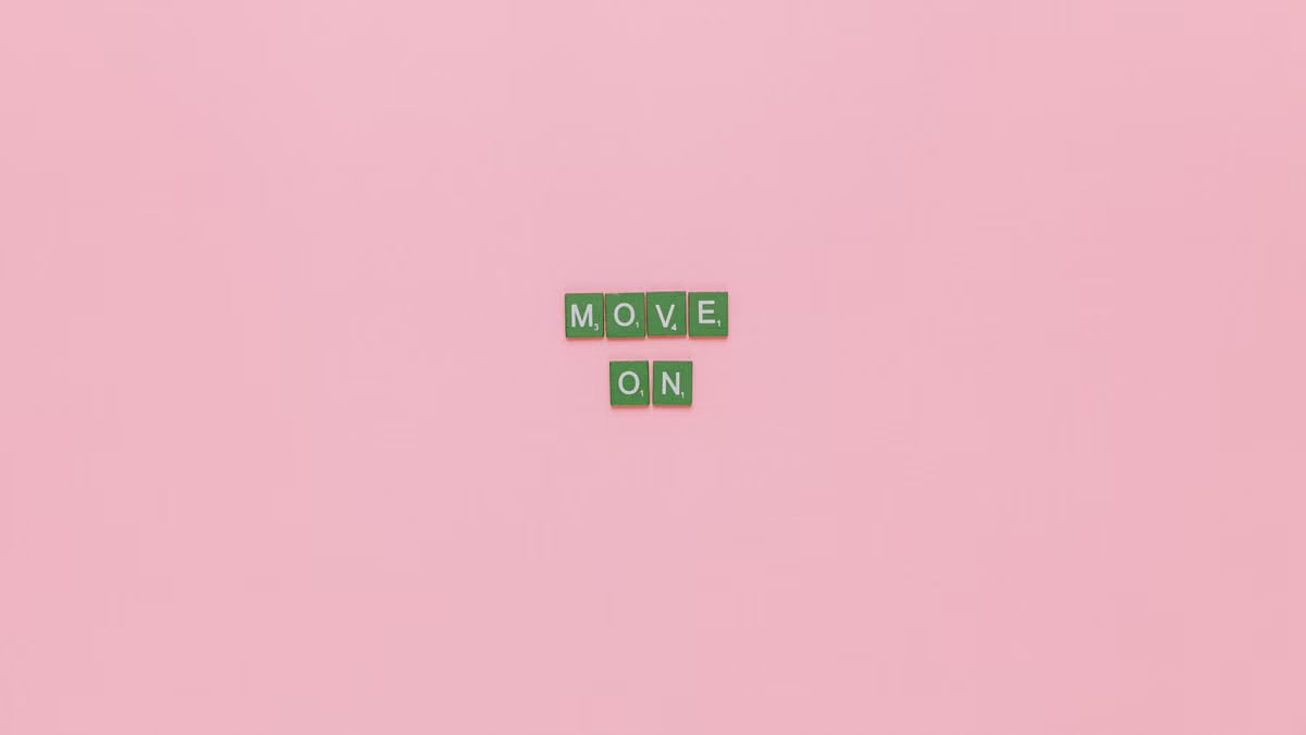 Inspirational text "Move On" spelled with green tiles on a pink background. Minimalist design, perfect for motivation.